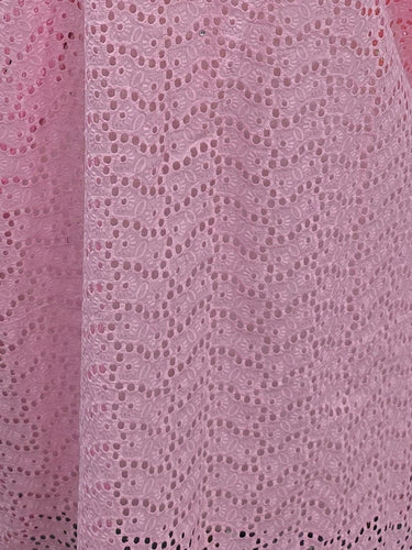 Pink knitted blanket with colorful stripes on a white shelf with various items.