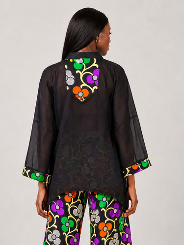 Full length view of an Ankara chiffon kaftan matching set featuring a multicolor floral African print in orange purple green and grey on a black background with dramatic wide sleeve kaftan overlay
