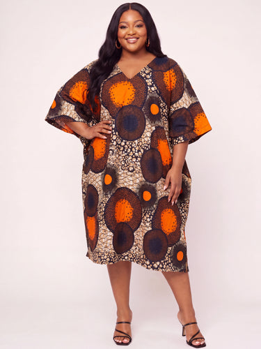 Plus size model wearing a bold orange navy and beige Ankara large scale circle medallion print midi dress with V neck wide kimono sleeves and relaxed kaftan silhouette styled with black strappy heeled sandals