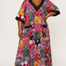 Plus size model wearing a vibrant Ankara patchwork maxi dress with black V neck trim and short kimono sleeves styled with gold heeled sandals against a white background