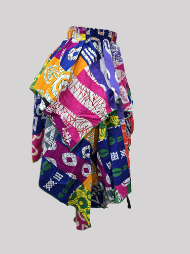 Plus size model wearing a vibrant multicolor Ankara patchwork midi skirt with elasticated high waist gathered ruffle waistband and handkerchief asymmetric hem styled with a black button down shirt and nude heeled sandals