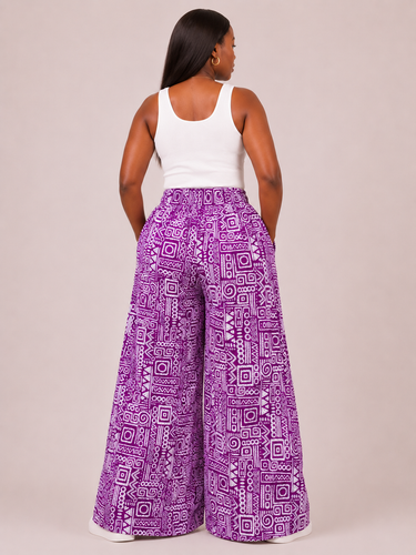 Person wearing purple patterned pants and a white top on a plain background