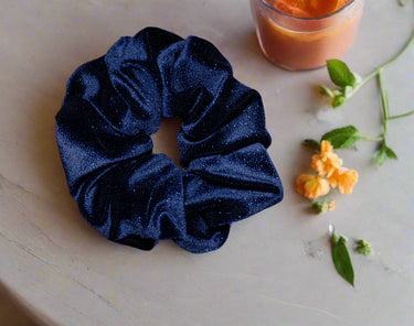 Navy blue glittery scrunchie in a black box with a pink label featuring 'SV'.